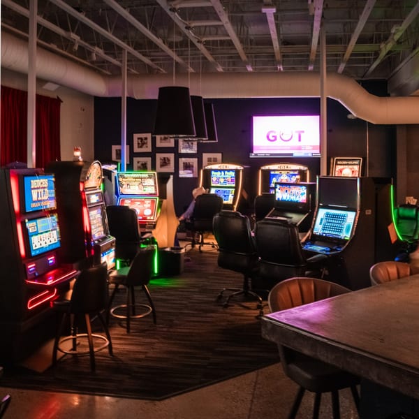 A dimly lit room with several glowing slot machines, chairs, and a large screen displaying "GOT".