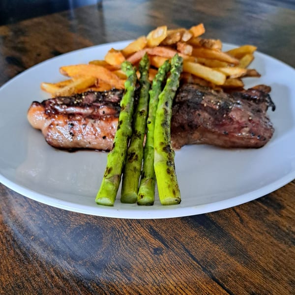 Grilled steak, asparagus, and golden french fries on a white plate, on a wooden table.