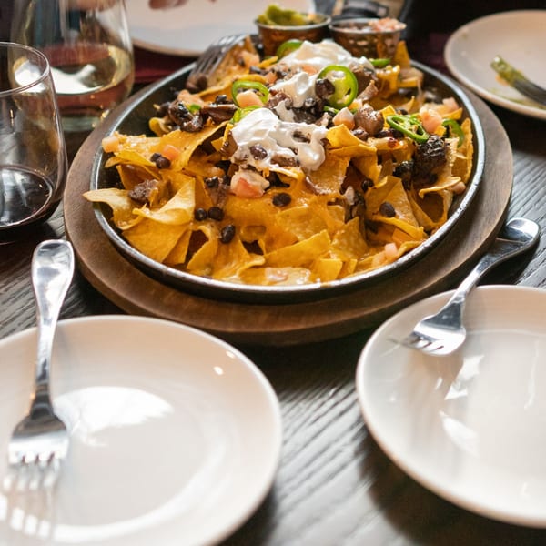 A sizzling platter of nachos with cheese, black beans, jalapeños, and sour cream.