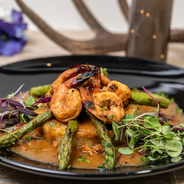 Grilled shrimp and asparagus served on a bed of rice with a rich sauce and microgreens.