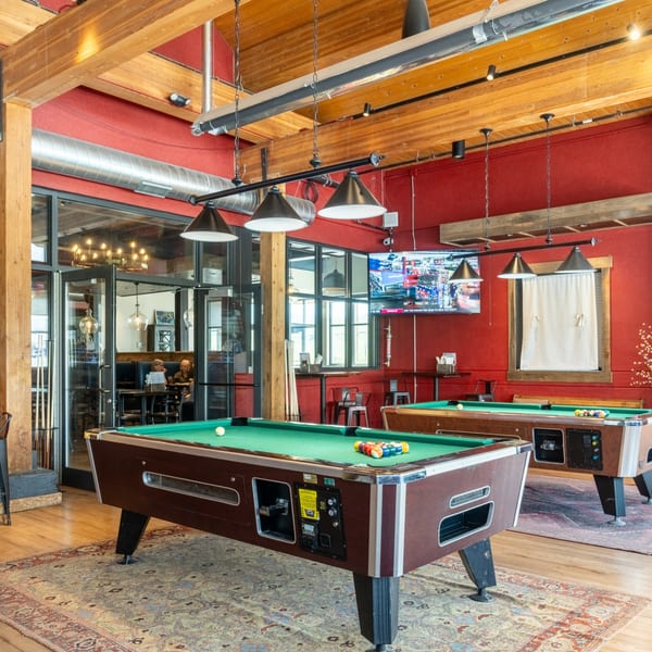 Two pool tables in a bar area with red walls, wooden beams, and a TV showing sports.